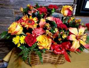 Woven basket with yellow, red, and orange flowers and greenery. Red bow on front.